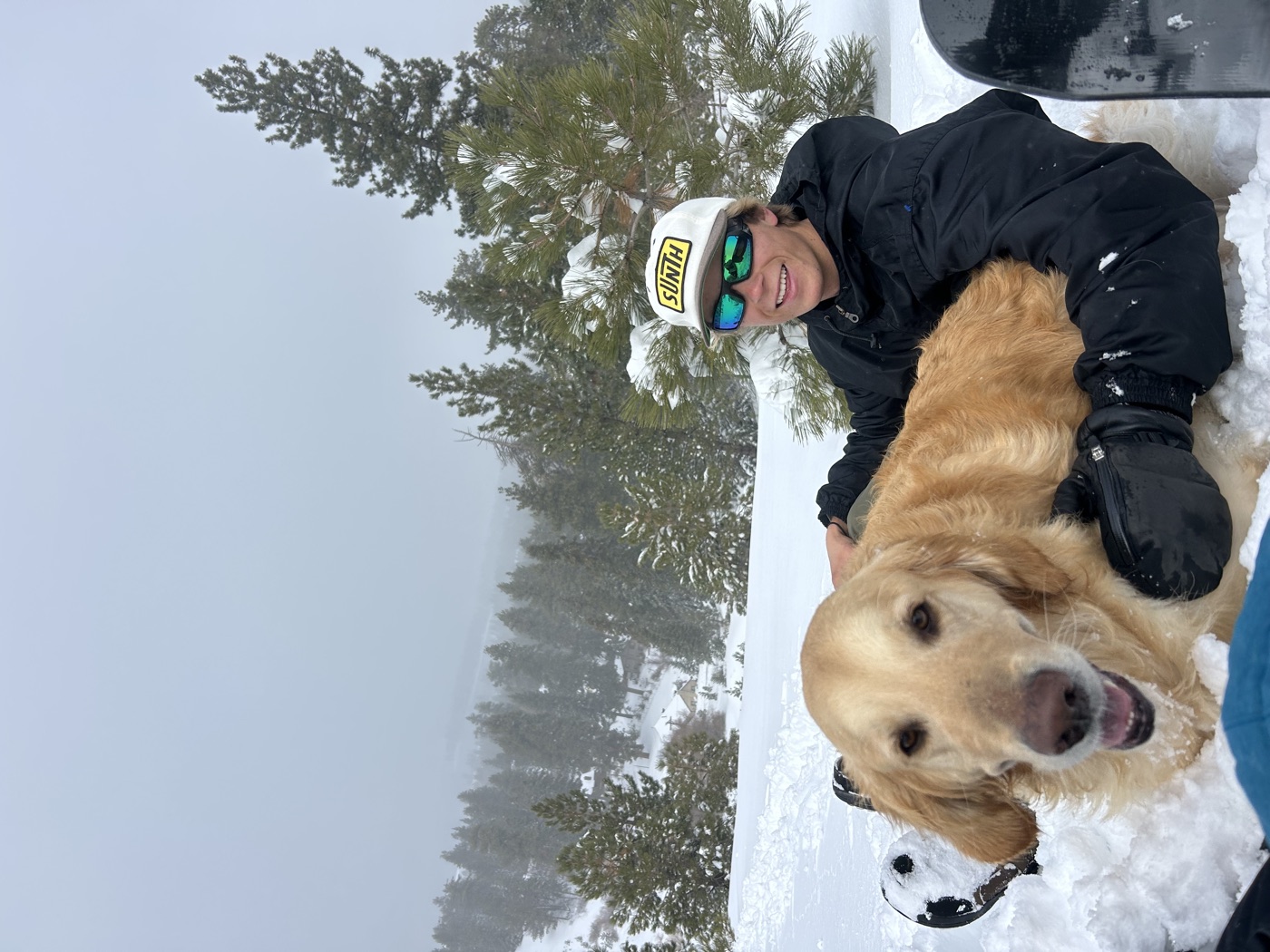 Kaiden in the snow with his golden retriever, wearing a custom trucker cap